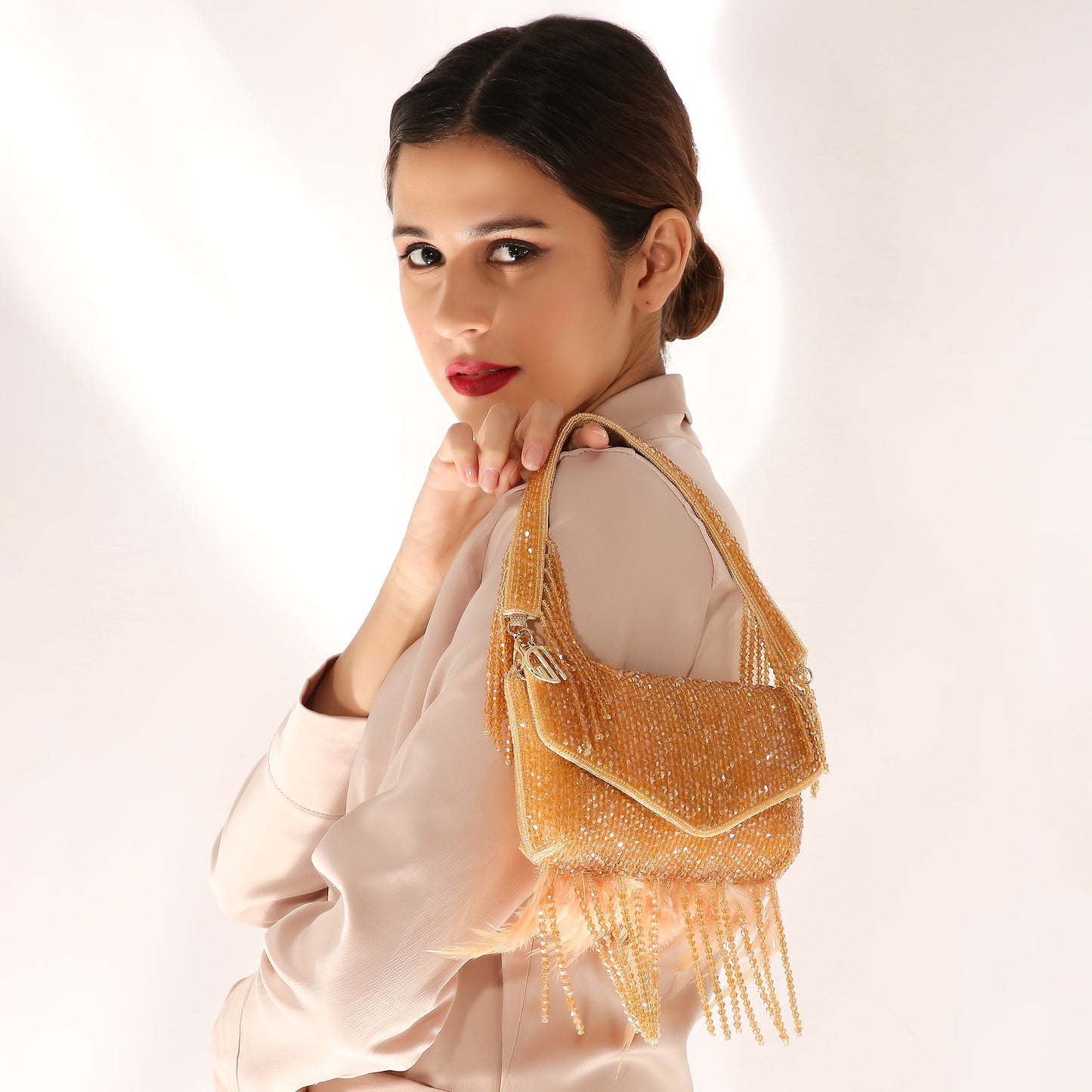 Woman holding a gold handbag with fringe details on a white background