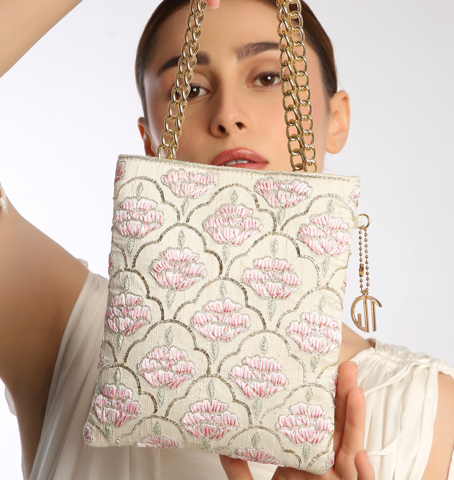 Woman holding a floral patterned handbag with a gold chain strap against a white background