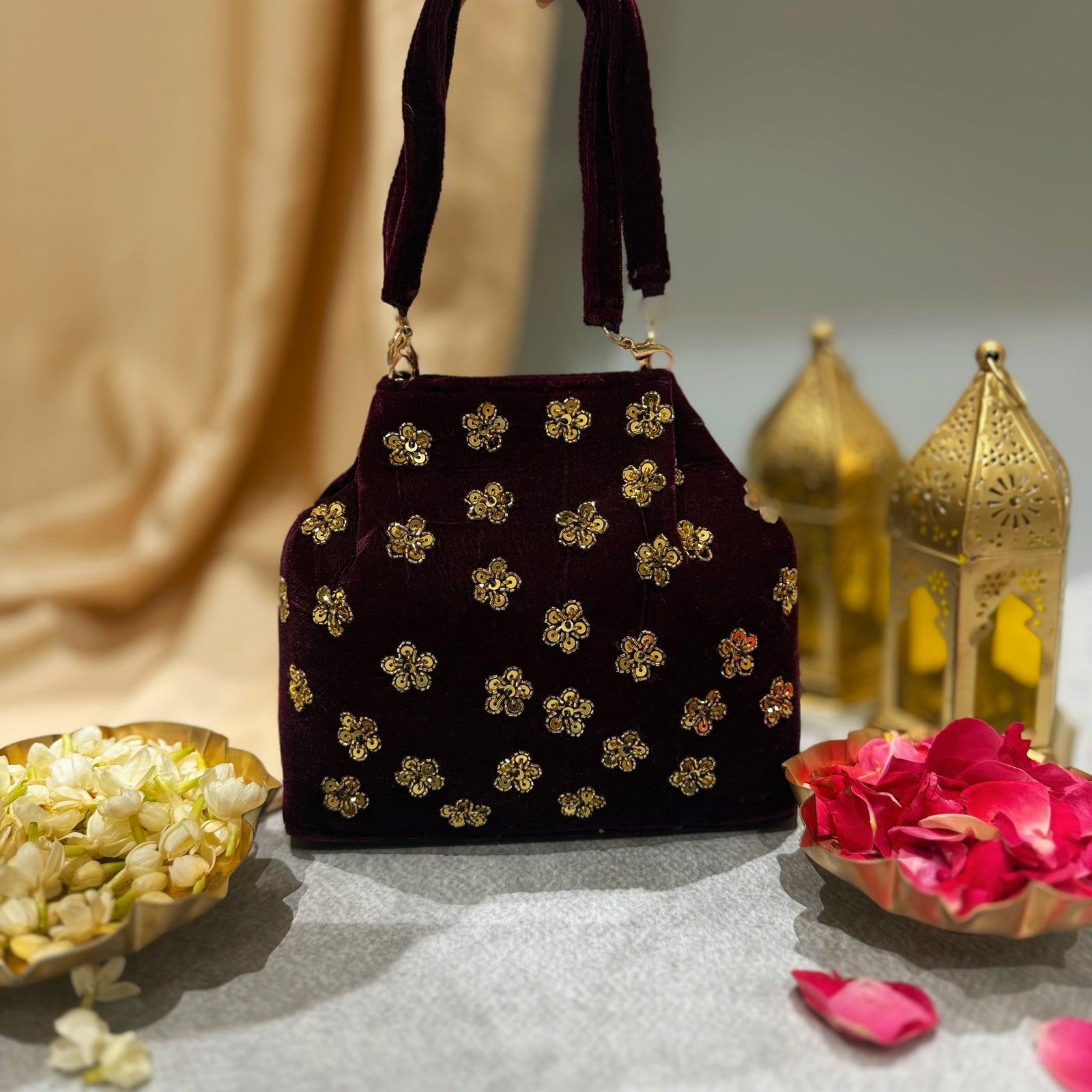 Maroon handbag with gold floral patterns on a neutral background with decorative elements.