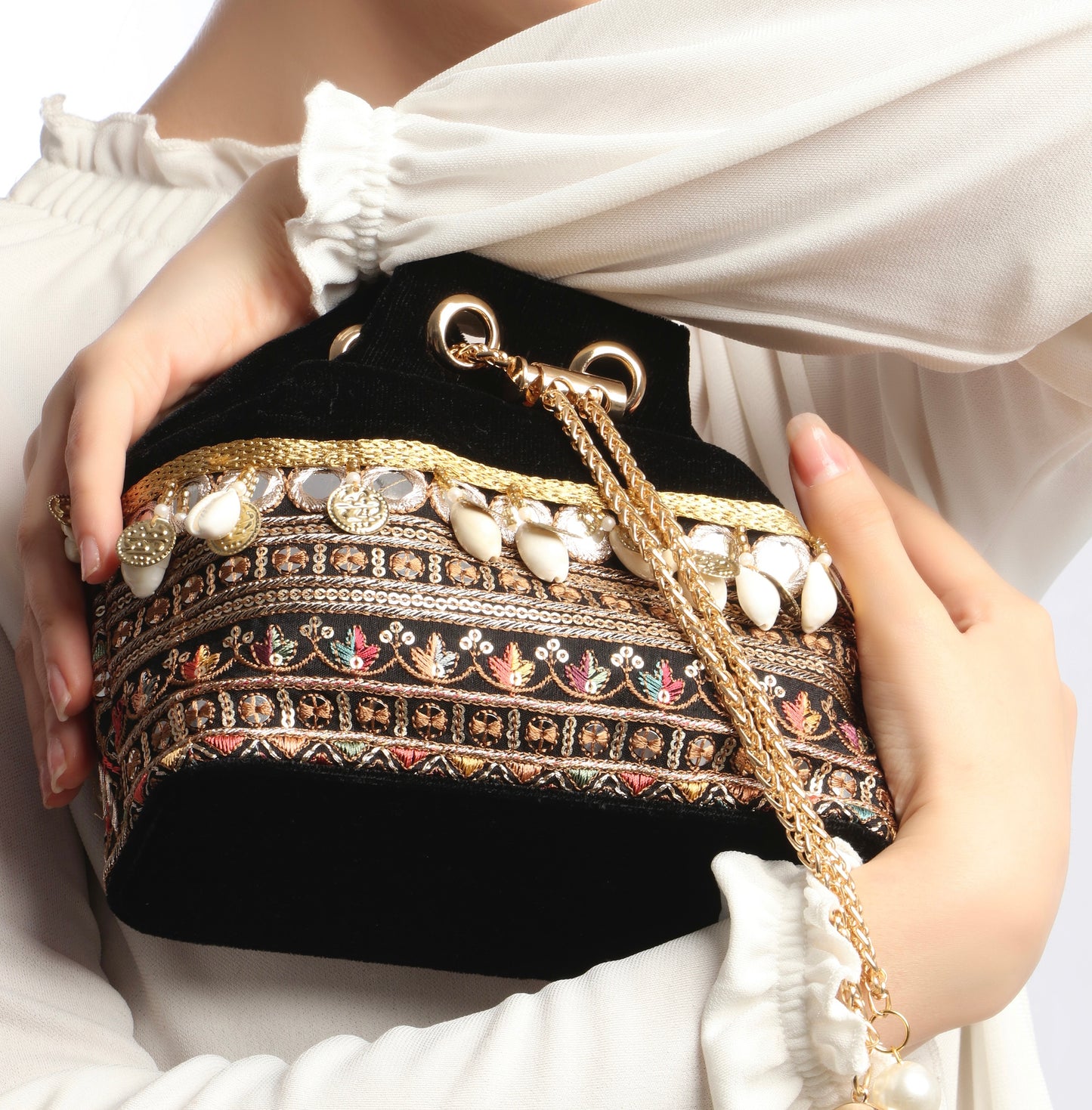 Black handbag with intricate gold and multicolor patterns held by a person wearing a white outfit.