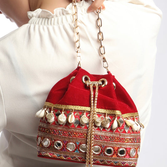 Red embroidered handbag with gold chain strap worn by a person in a white outfit.